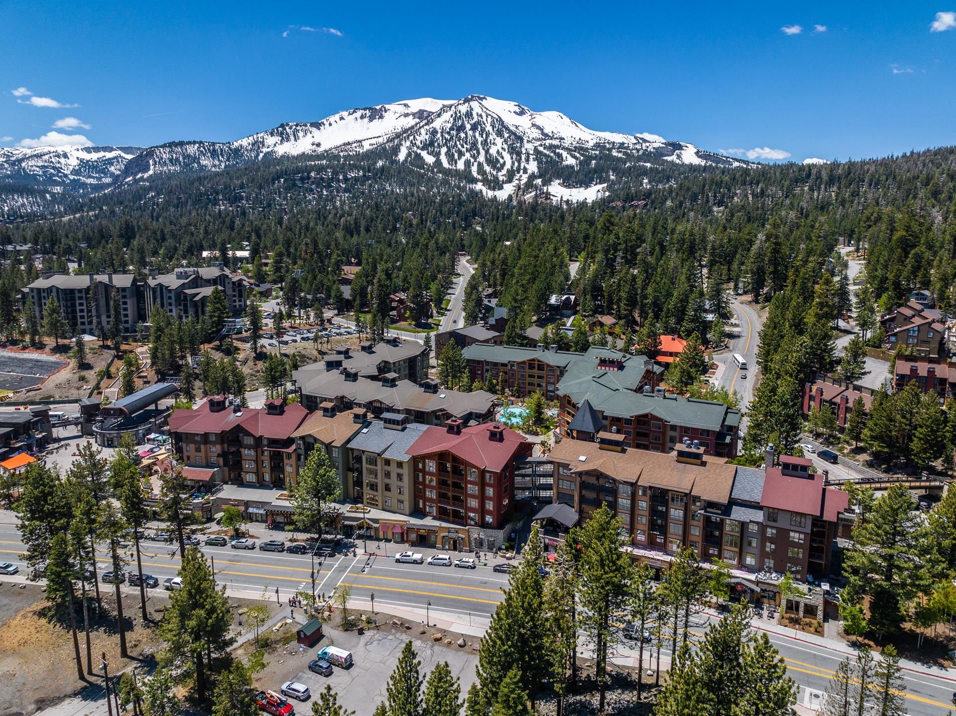 6201 Minaret Road, Unit 2221 Mammoth Lakes, CA 93546 - Photo 37 of 44 Aerial perspective showcasing multiple buildings nestled among dense evergreen forests, with a prominent snow-capped mountain range in the background