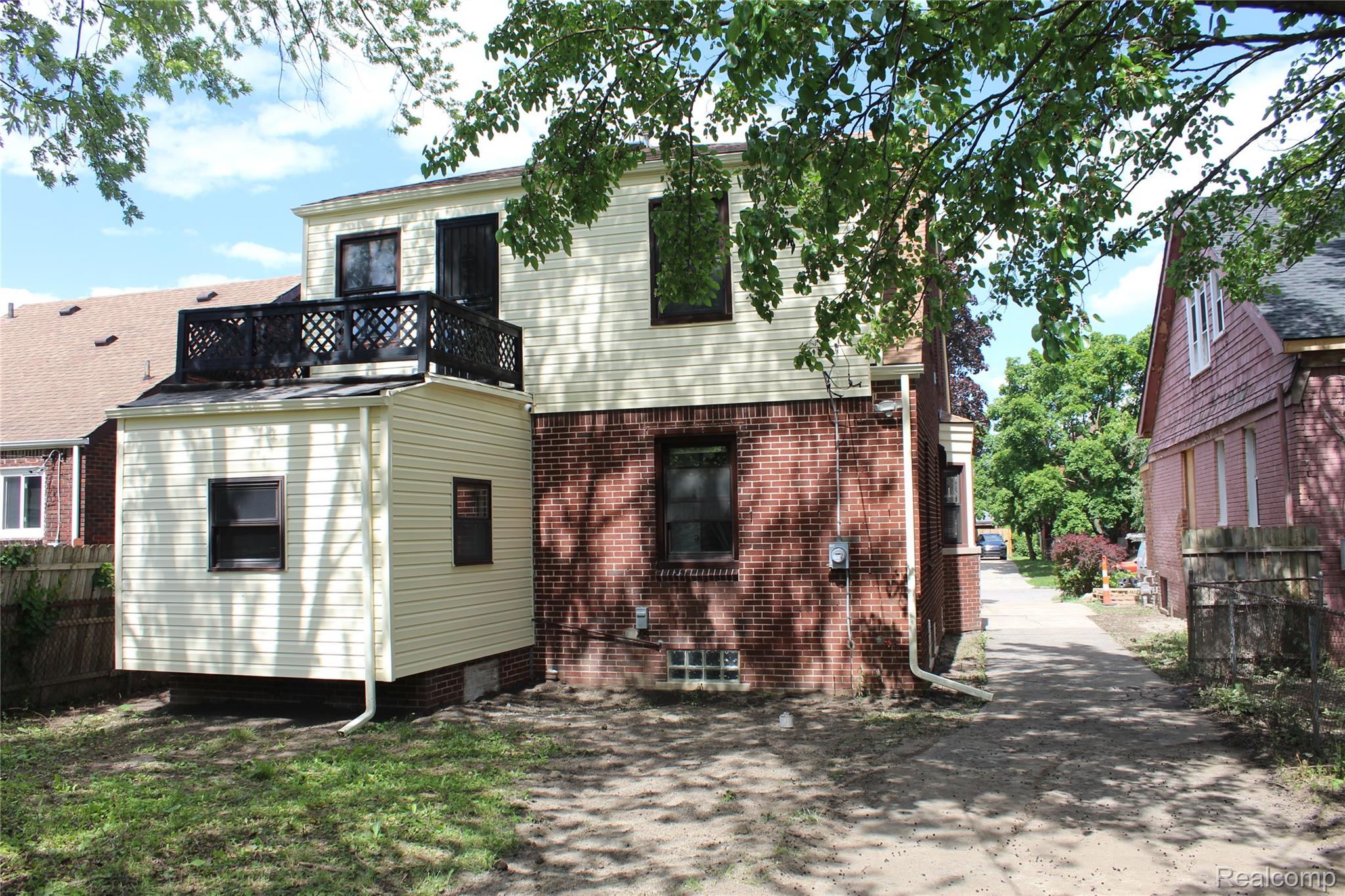 5543 Balfour Road Detroit, MI 48224 - Photo 4 of 54 Rear exterior featuring brick and light-colored siding, a second-story balcony with lattice railing, and a windowed ground-level addition