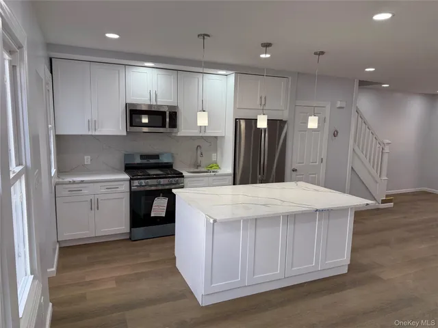a kitchen with stainless steel appliances kitchen island a sink dishwasher a refrigerator and a stove with wooden floor