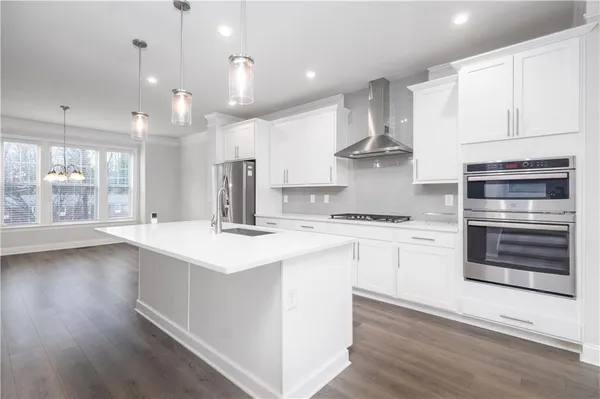 a kitchen with kitchen island granite countertop a stove a sink and white cabinets with wooden floor