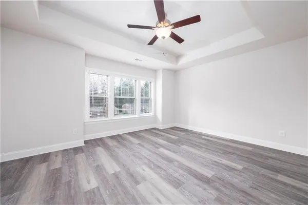 an empty room with wooden floor ceiling fan and windows