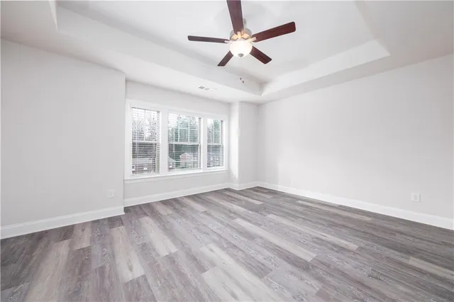 an empty room with wooden floor ceiling fan and windows