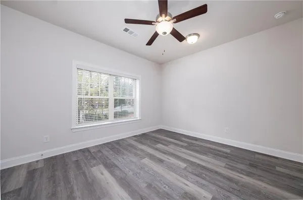 an empty room with wooden floor ceiling fan and windows
