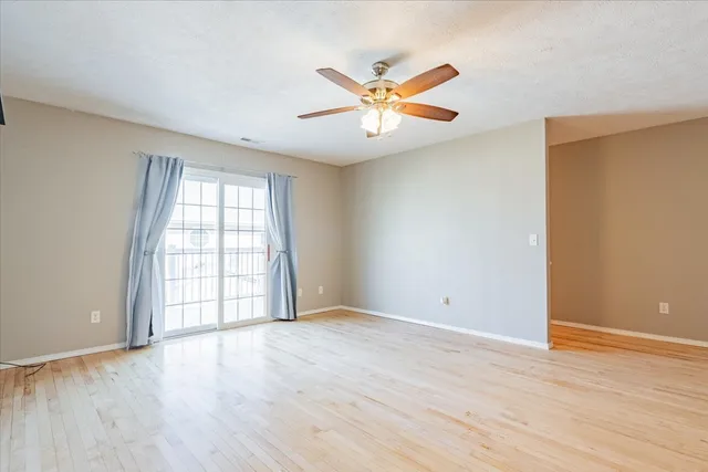 an empty room with wooden floor fan and windows