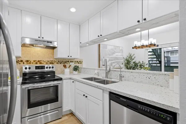 a kitchen with stainless steel appliances a stove a sink and white cabinets