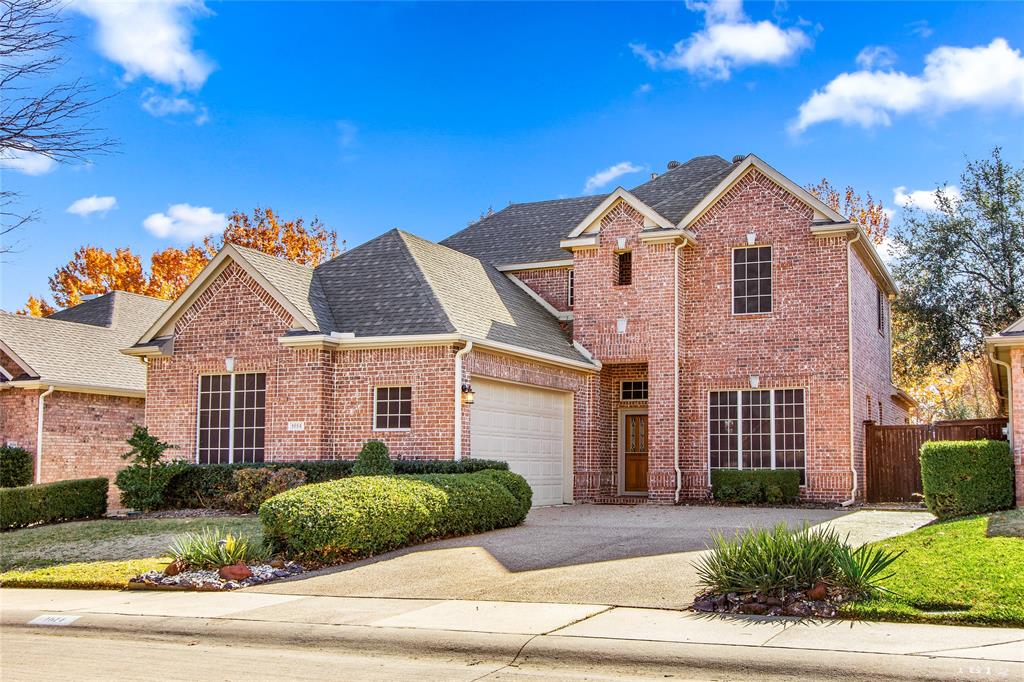 Traditional-style home featuring a shingled roof, brick siding, driveway, and an attached garage