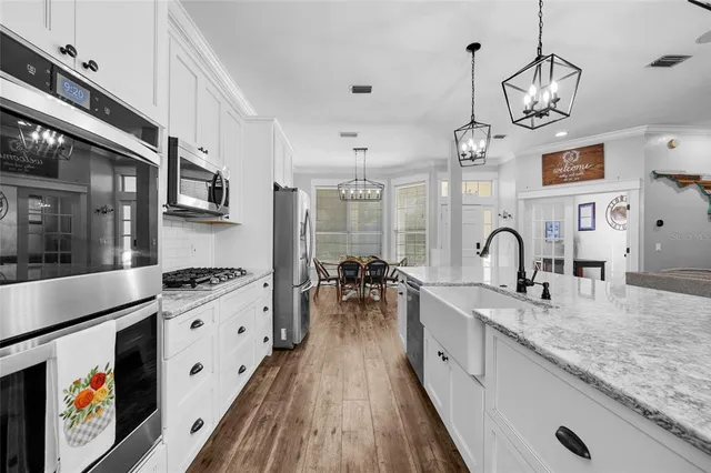 a kitchen with stainless steel appliances granite countertop a stove a sink dishwasher and white cabinets with wooden floor