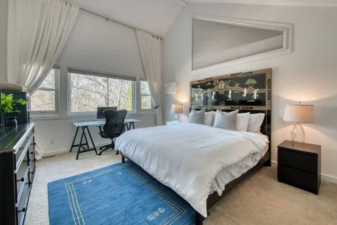 a bedroom with a bed a table and large windows