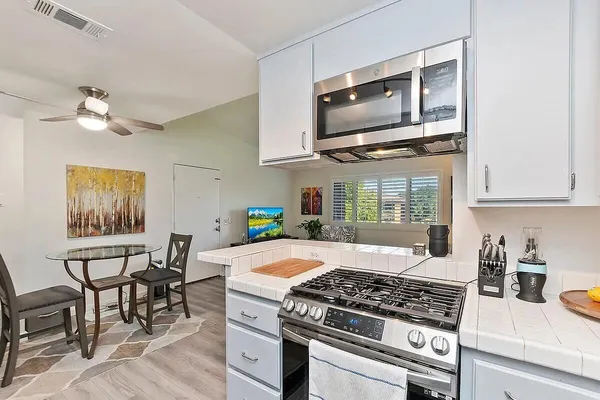 a kitchen with stainless steel appliances granite countertop a stove top oven a sink a dining table and chairs with wooden floor