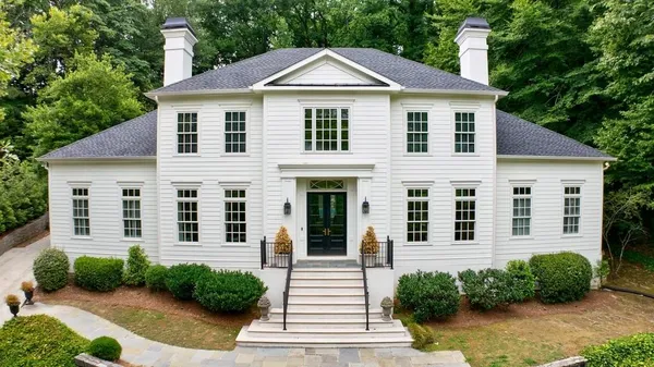 a view of a white house with a small yard plants and large tree