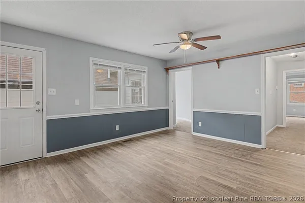 a view of an empty room with wooden floor and a ceiling fan