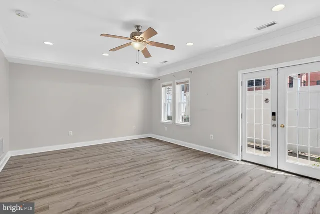 a view of an empty room with wooden floor and a ceiling fan