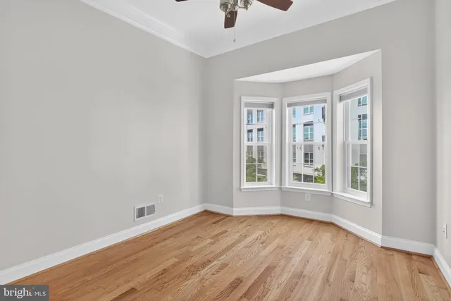 an empty room with wooden floor fan and windows