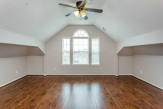 an empty room with wooden floor a chandelier fan and windows