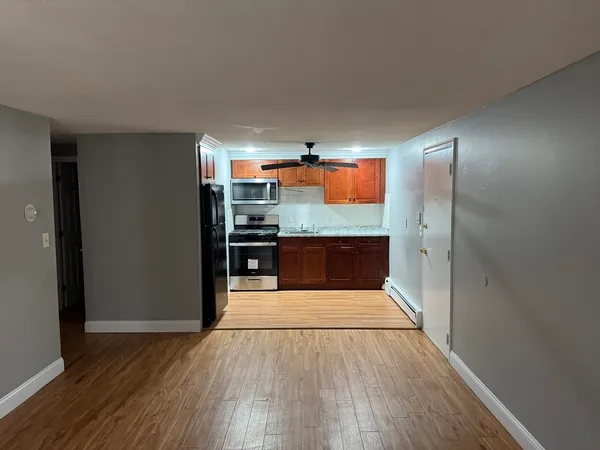 an empty room with wooden floor and way to kitchen