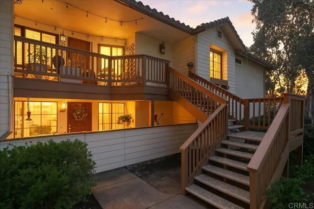 a view of a house with wooden stairs and a large tree front of it