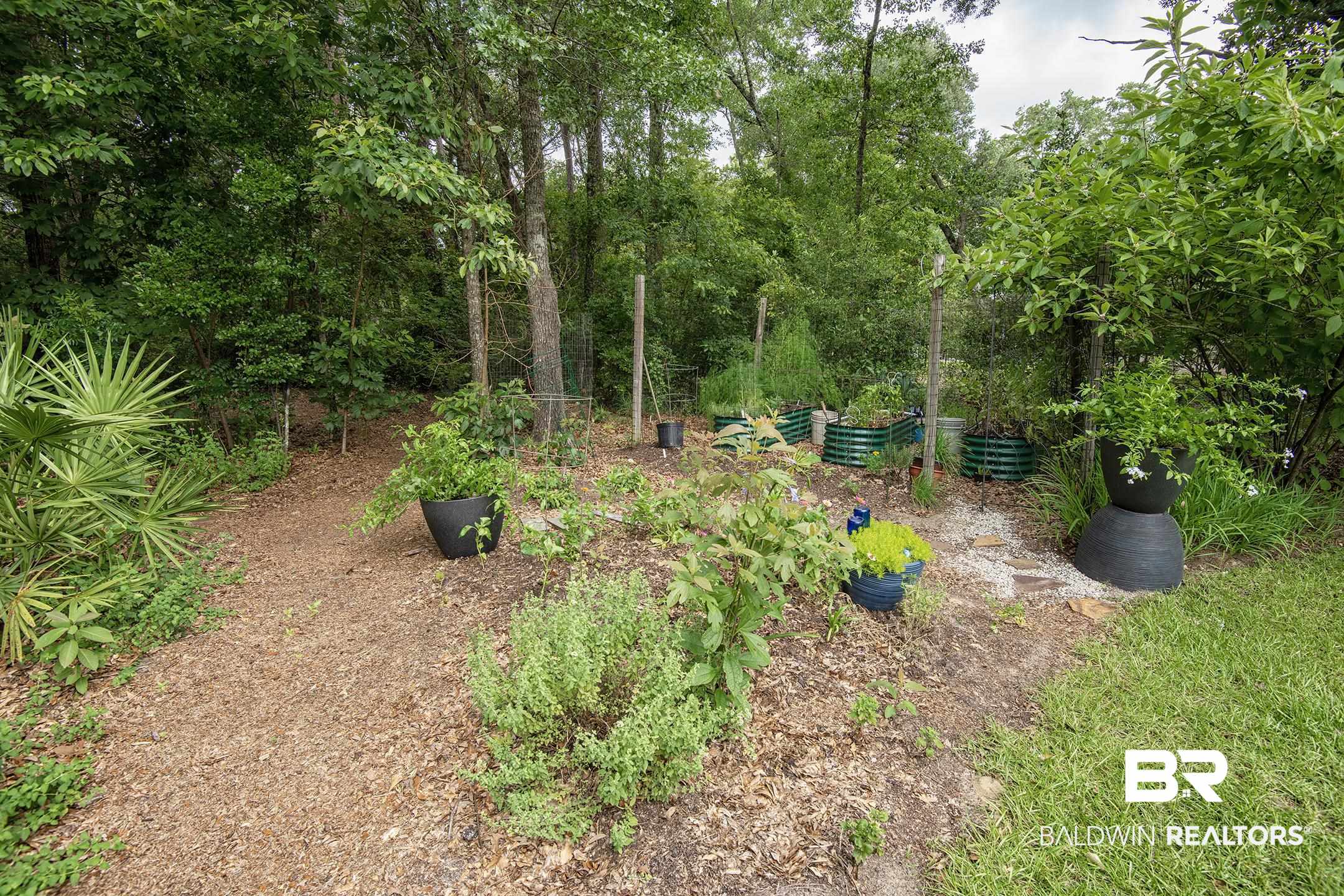 18754 Treasure Oaks Road Gulf Shores, AL 36542 - Photo 43 of 53 Expansive garden area featuring multiple planted beds, mature trees, and a mulched pathway