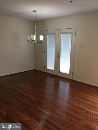 an empty room with wooden floor chandelier and windows