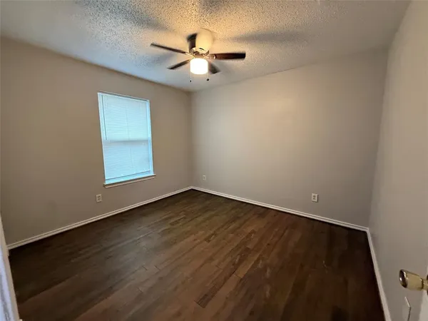 an empty room with wooden floor fan and window