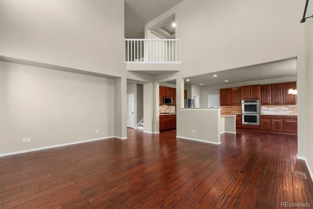 a view of an empty room with wooden floor and a kitchen