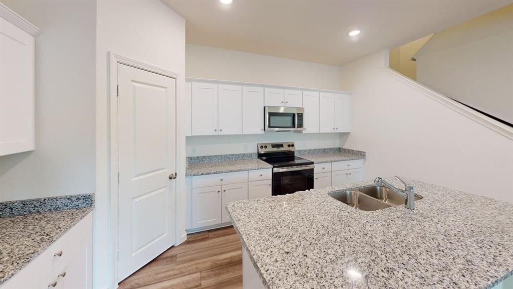 4529 Winecup Road Melissa, TX 75454 - Photo 3 of 29 Kitchen featuring a center island with a double basin sink, stone-finish countertops, extensive white cabinetry, stainless steel appliances, and wood-finish flooring