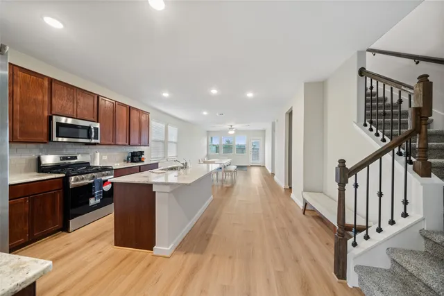 a kitchen with stainless steel appliances granite countertop a refrigerator a stove top oven a sink dishwasher and wooden cabinets with wooden floor