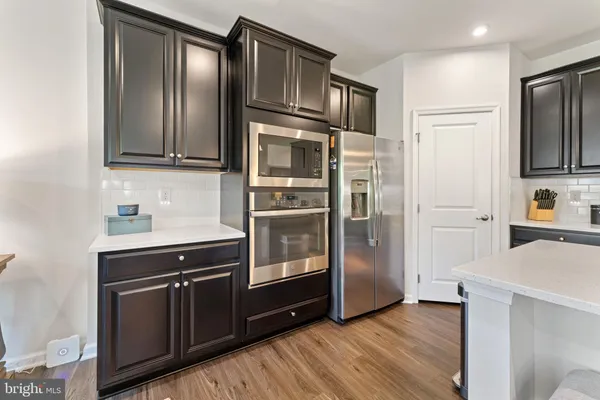 a kitchen with stainless steel appliances kitchen island granite countertop a refrigerator a stove a sink a dining table and chairs with wooden floor