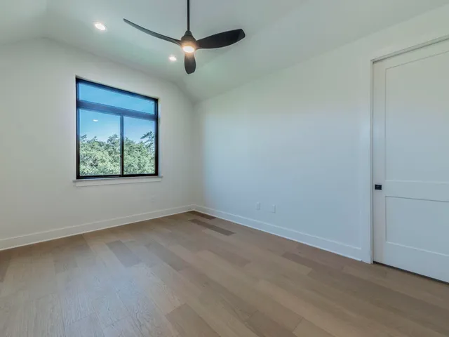 an empty room with wooden floor ceiling fan and windows