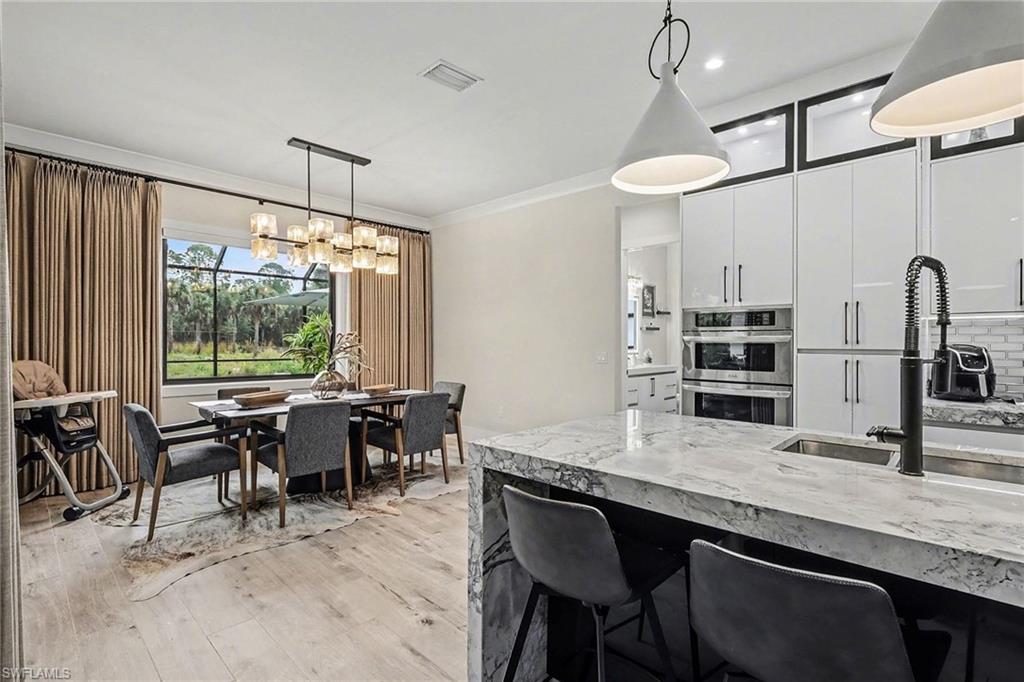 1720 21st Street Southwest Naples, FL 34117 - Photo 12 of 42 Kitchen with light stone counters, decorative light fixtures, white cabinets, crown molding, and light wood finished floors