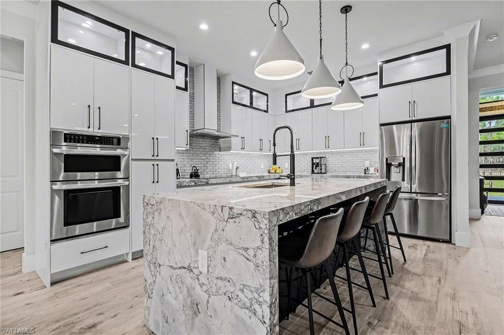 1720 21st Street Southwest Naples, FL 34117 - Photo 14 of 42 Kitchen with hanging light fixtures, white cabinetry, a breakfast bar, appliances with stainless steel finishes, and a center island with sink