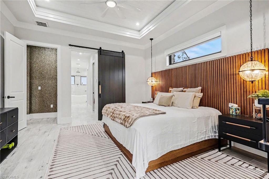 1720 21st Street Southwest Naples, FL 34117 - Photo 17 of 42 Bedroom featuring a barn door, light wood-style flooring, ensuite bath, wooden walls, and ceiling fan