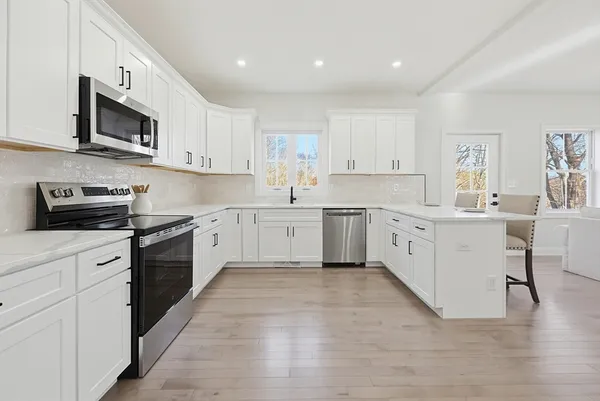 a large white kitchen with stainless steel appliances granite countertop a stove top oven a sink dishwasher and white cabinets with wooden floor