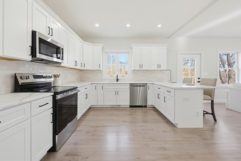 673 Pleasant Street Leicester, MA 01542 - Photo 11 of 38 a large white kitchen with stainless steel appliances granite countertop a stove top oven a sink dishwasher and white cabinets with wooden floor