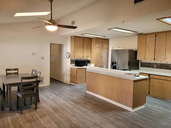 a kitchen with stainless steel appliances kitchen island granite countertop a table chairs refrigerator and microwave