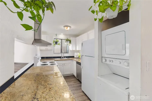 a white kitchen with a stove a faucet a potted plant a large window and a glass door