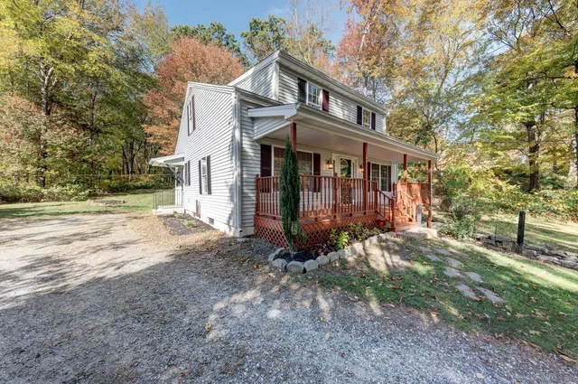 a view of a white house that has a small yard and large trees