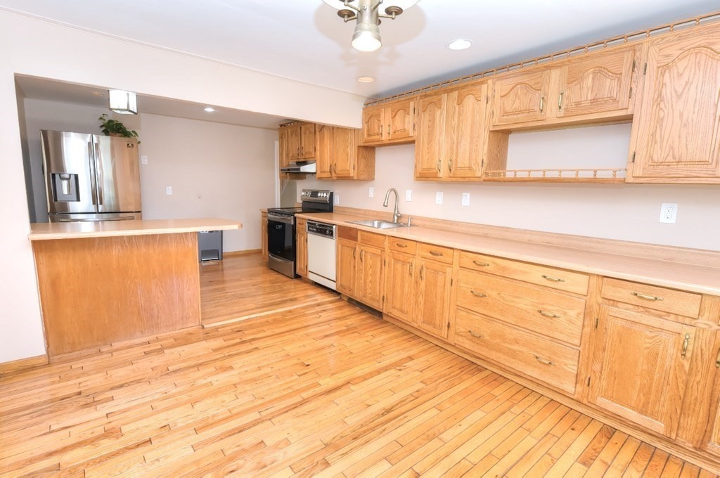 165 R Green Street Stoneham, MA 02180 - Photo 12 of 42 a large kitchen with granite countertop a stove a sink dishwasher and white cabinets with wooden floor