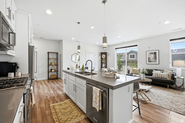 3355 Santa Fe Road Park City, UT 84098 - Photo 6 of 45 Open-concept kitchen featuring an island with a built-in sink and pendant lighting, stainless steel appliances, wood-finish flooring, white cabinetry, and recessed lighting