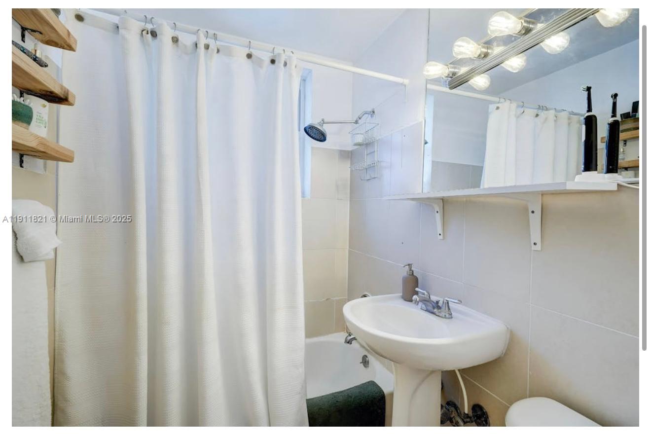320 80th Street, Unit 15 Miami Beach, FL 33141 - Photo 4 of 6 a bathroom with a sink a mirror and a shower curtain