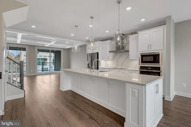 a kitchen with stainless steel appliances granite countertop a refrigerator a sink dishwasher a oven and a dining table with wooden floor