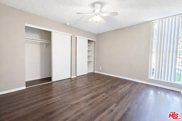 an empty room with wooden floor chandelier fan and windows