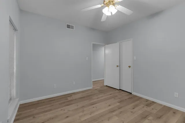 a view of an empty room with wooden floor and a ceiling fan