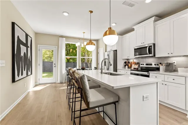 a kitchen with stainless steel appliances granite countertop a stove a sink a microwave a refrigerator a dining table and chairs with wooden floor