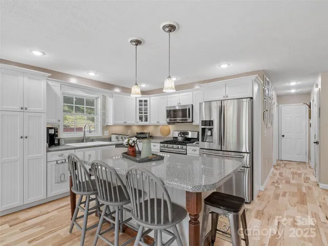 a kitchen with stainless steel appliances granite countertop a dining table chairs stove refrigerator and cabinets