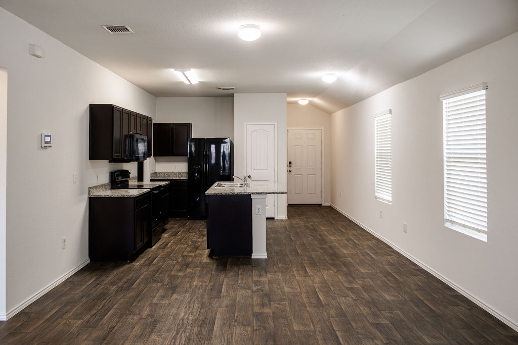 14915 Talus Road Manor, TX 78653 - Photo 3 of 20 Rich wood-look flooring anchors this open kitchen layout featuring dark cabinetry and a central island.