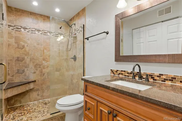 a bathroom with a granite countertop sink a toilet a mirror and shower
