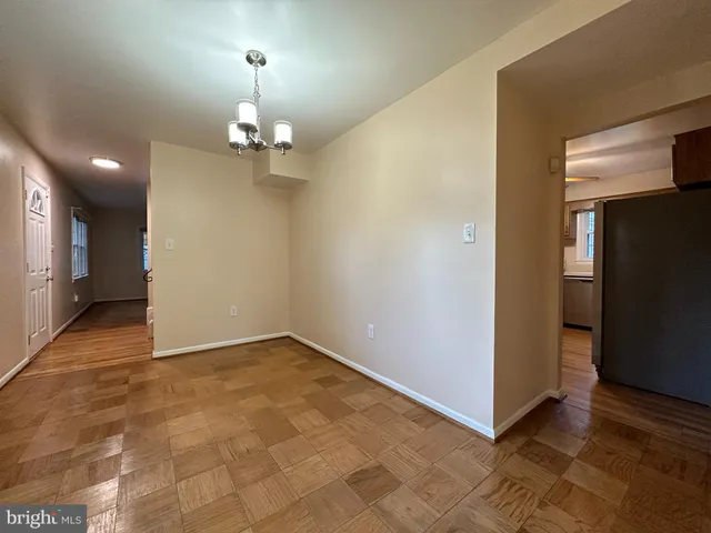 an empty room with chandelier fan and kitchen view