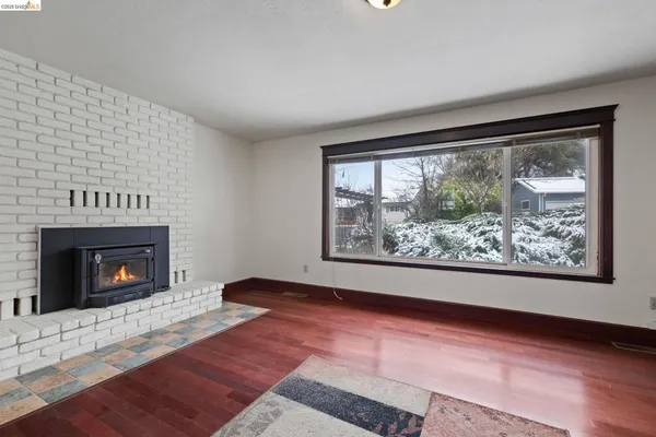 a view of an empty room with wooden floor fireplace and a window