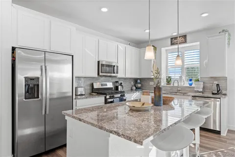 a kitchen with stainless steel appliances granite countertop a refrigerator a sink a stove a table and chairs