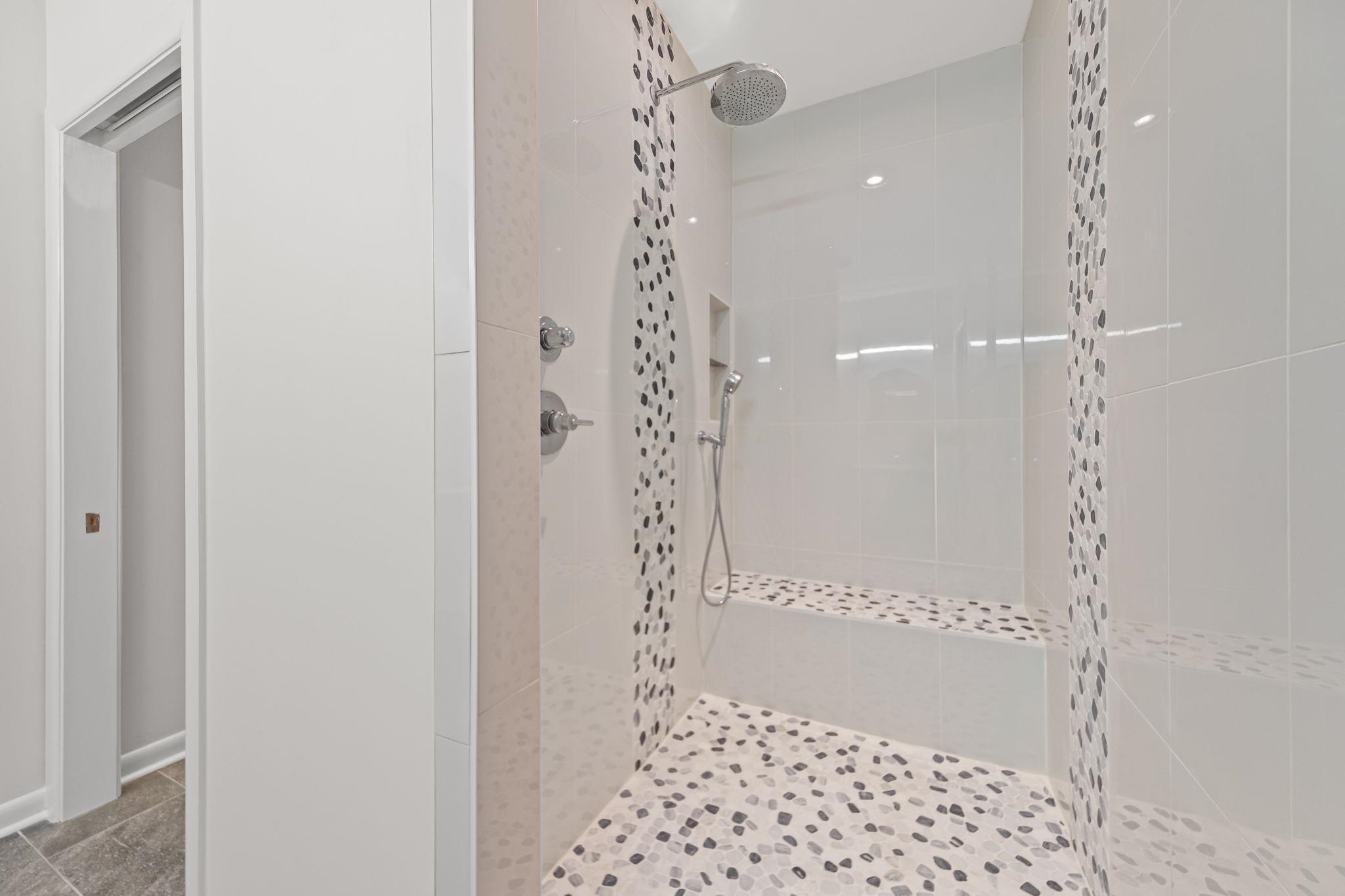 448 Tennessee Street Memphis, TN 38103 - Photo 16 of 39 Walk-in shower featuring a rainfall showerhead, handheld sprayer, built-in bench, recessed shelf, and natural pebble tile flooring with coordinating accent stripes